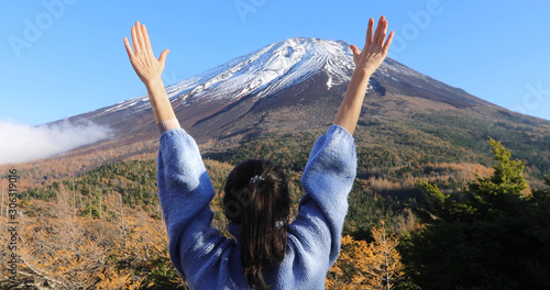 Back view of woman in warm sweater raising hands enjoying mountain Fuji view in bright day