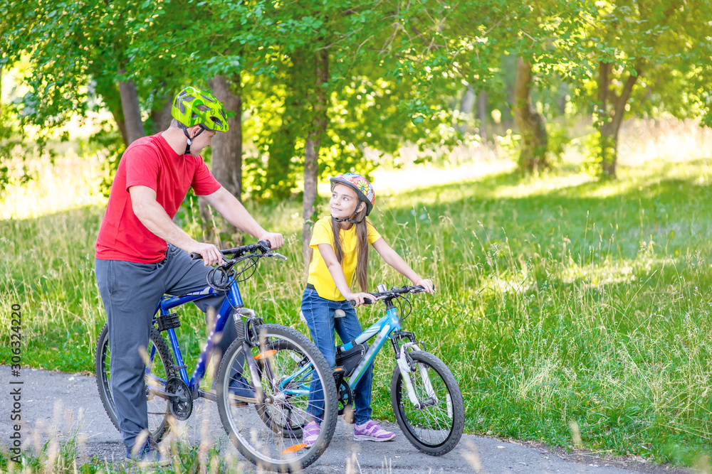 Obraz premium Father and her daughter cycling in the summer park together. Empty space for text
