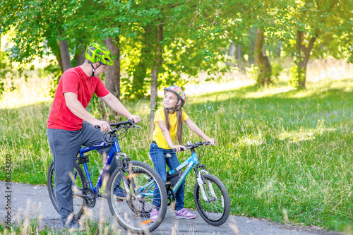 Father and her daughter cycling in the summer park together. Empty space for text