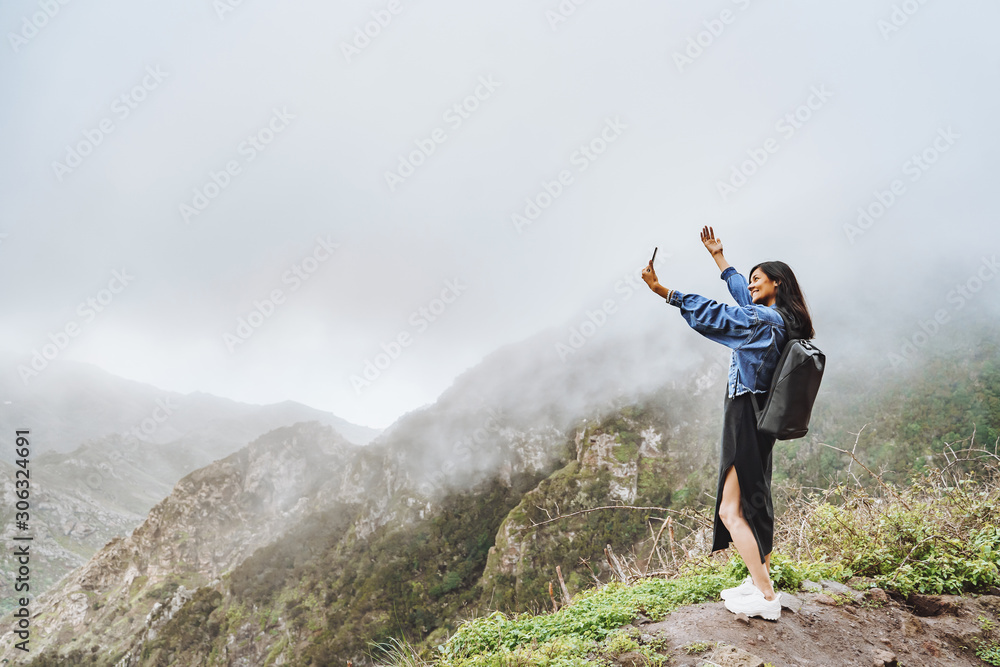 Happy woman tourist taking selfie using smartphone on top of a mountain Happy woman tourist taking selfie using smartphone on top of a mountain