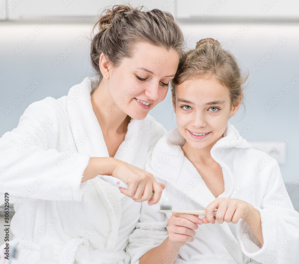 Smiling mother squeezes toothpaste onto toothbrush for daughter in bathroom at home Smiling mother squeezes toothpaste onto toothbrush for daughter in bathroom at home