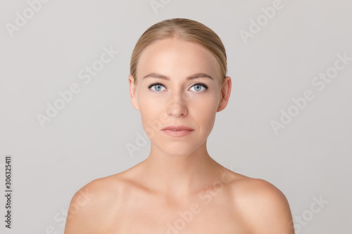 Portrait of beautiful young blonde with natural makeup looking aside and posing on white isolated background. Naked female model without accessories in studio. Concept of beauty and tenderness.