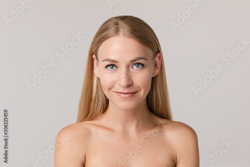 Medium close-up portrait of beautiful young European woman isolated at white studio background. Charming smiling naked female with long blonde hair looking at camera having positive emotion