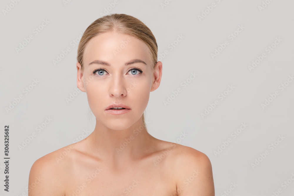 Studio portrait of attractive blonde caucasian woman with blue eyes and bare shoulders over white background. She is looking at camera with eyes wide open. Pure, smooth and flawless skin concept. Studio portrait of attractive blonde caucasian woman with blue eyes and bare shoulders over white background. She is looking at camera with eyes wide open. Pure, smooth and flawless skin concept.