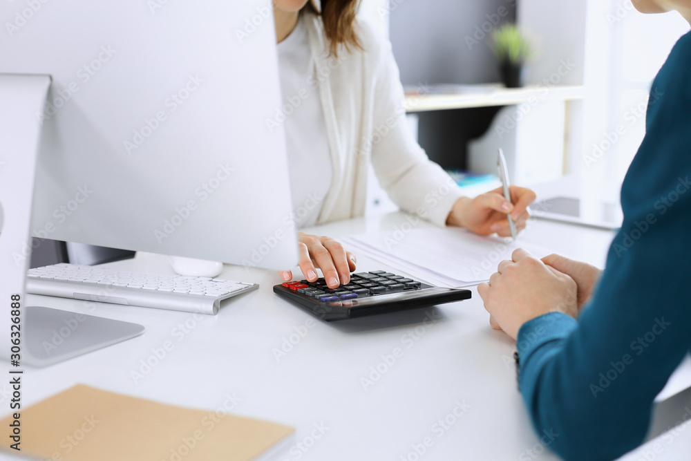 Accountant checking financial statement or counting by calculator income for tax form, hands close-up. Business woman sitting and working with colleague at the desk in office. Audit concept Accountant checking financial statement or counting by calculator income for tax form, hands close-up. Business woman sitting and working with colleague at the desk in office. Audit concept