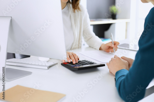 Accountant checking financial statement or counting by calculator income for tax form, hands close-up. Business woman sitting and working with colleague at the desk in office. Audit concept