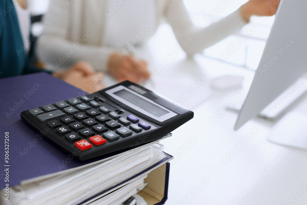 Calculator and binders with papers are waiting to be processed by business woman or bookkeeper working at the desk in office back in blur. Internal Audit and tax concept Calculator and binders with papers are waiting to be processed by business woman or bookkeeper working at the desk in office back in blur. Internal Audit and tax concept