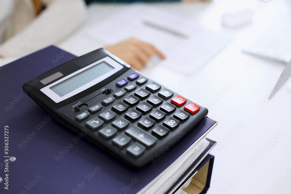 Calculator and binders with papers are waiting to be processed by business woman or bookkeeper working at the desk in office back in blur. Internal Audit and tax concept Calculator and binders with papers are waiting to be processed by business woman or bookkeeper working at the desk in office back in blur. Internal Audit and tax concept