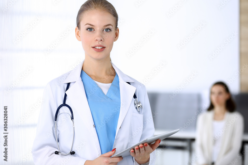 Doctor woman filling up medication history record while standing in emergency hospital office with patient in queue at background. Physician at work, portrait shoot. Medicine and health care concept Doctor woman filling up medication history record while standing in emergency hospital office with patient in queue at background. Physician at work, portrait shoot. Medicine and health care concept
