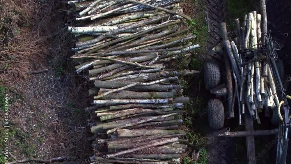 Top down aerial view of a tractor using a grab to load a stack of wood lengths onto the trailer with room for text. Top down aerial view of a tractor using a grab to load a stack of wood lengths onto the trailer with room for text.