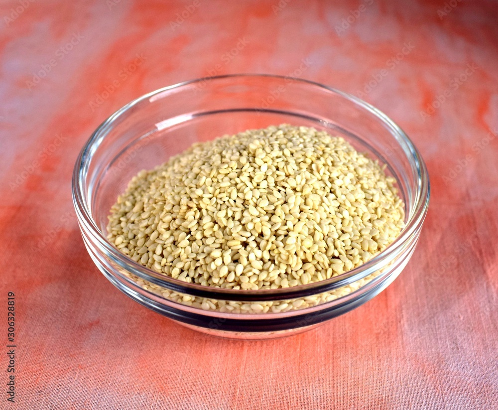 sesame seeds in a transparent bowl on a reddish tablecloth sesame seeds in a transparent bowl on a reddish tablecloth