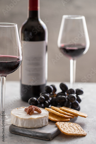 Red wine bottle with wine glass and charcuterie board with different snacks for wine. French Cheese, grapes and crackers.