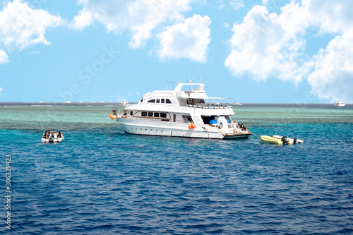 Modern Egyptian Diving Boat In The Sea Near Coral Reef Island. White Marine Pleasure Craft With Tourists In The Red Sea. Entertaining Boat Trip. Calm Blue Sea And Clouds.