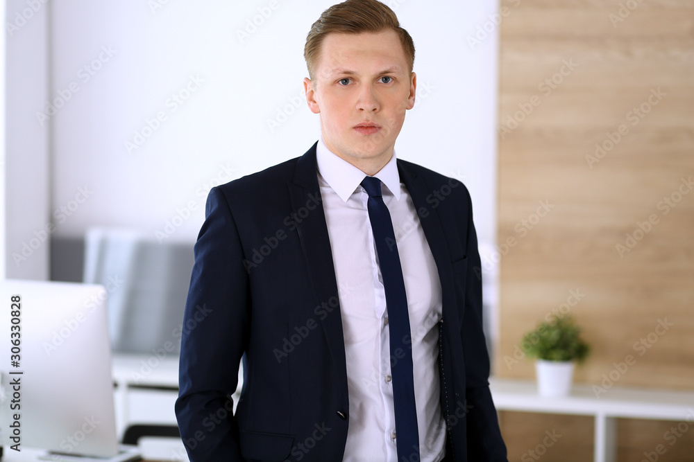 Cheerful businessman standing and looking at camera in office. Headshot of young and successful entrepreneur. Business concept