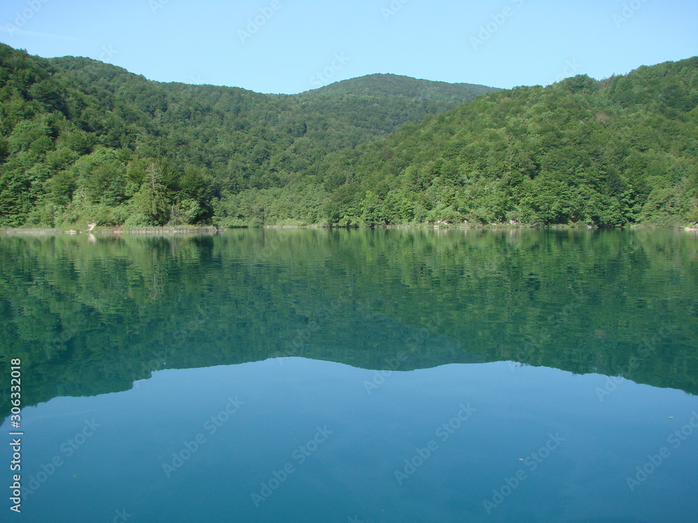 View from the deck of the ship on the quiet azure surface of the lake surrounded by mountain forest that densely covers its shores.