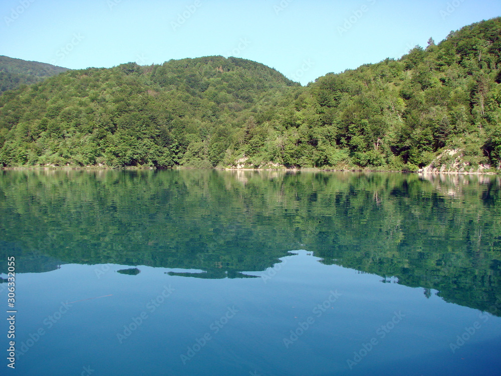 View from the deck of the ship on the quiet azure surface of the lake surrounded by mountain forest that densely covers its shores.