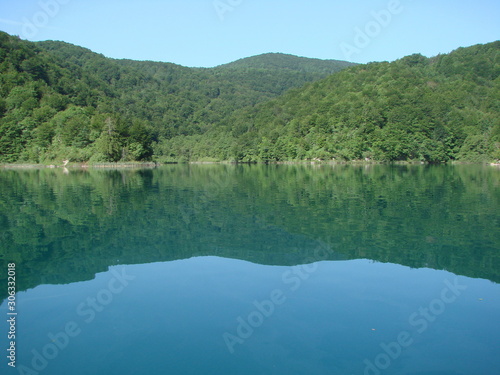 View from the deck of the ship on the quiet azure surface of the lake surrounded by mountain forest that densely covers its shores.