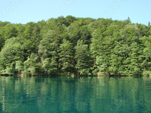 View from the deck of the ship on the quiet azure surface of the lake surrounded by mountain forest that densely covers its shores.