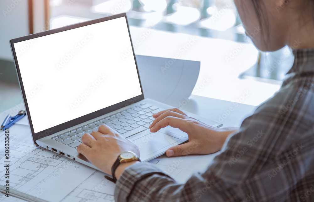 Woman designer of architect sitting and pointing and design a project are working on laptop of white mockup display with a blueprint and Model in the office Woman designer of architect sitting and pointing and design a project are working on laptop of white mockup display with a blueprint and Model in the office