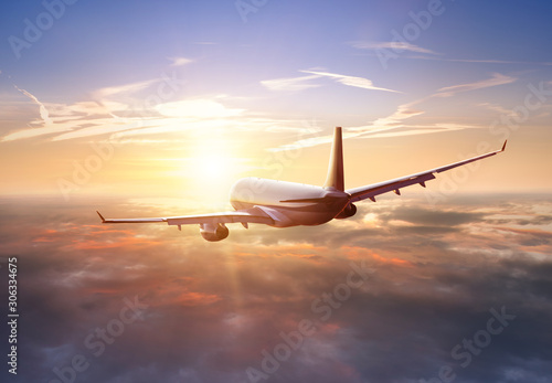 Fototapeta Naklejka Na Ścianę i Meble -  Passengers commercial airplane flying above clouds in sunset light. Concept of fast travel, holidays and business.