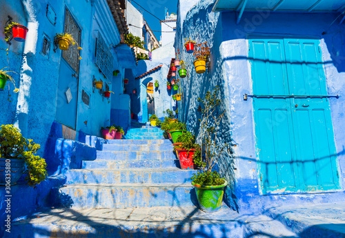 Pretty narrow street with blue walls, stairs and colorful flowerpots in Chefchaouen, Morocco © leelook