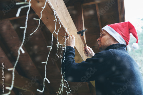 Foto man with santa hat decorating house outdoor carport with christmas string lights