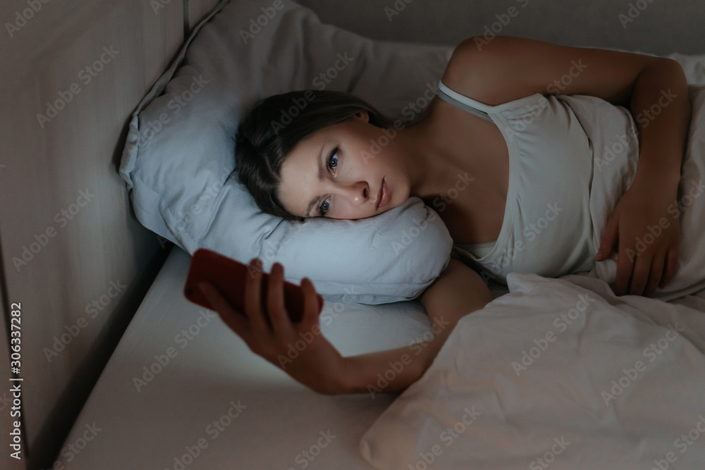 Female using her smartphone in bed at night instead sleeping. Phone and social network addicted. Gadget dependence concept Female using her smartphone in bed at night instead sleeping. Phone and social network addicted. Gadget dependence concept