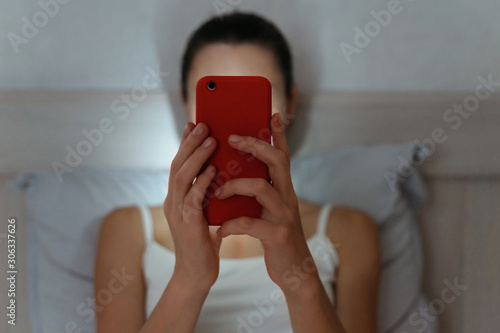 Young female browsing with smartphone late at night. Focused on cellphone. Intermet and social network dependence concept photo