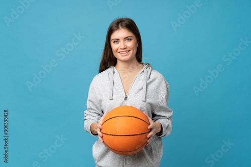 Young woman over isolated blue background with ball of basketball