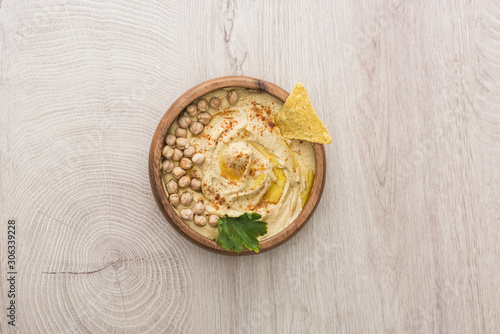 top view of delicious hummus with chickpeas and nacho in bowl on beige wooden table