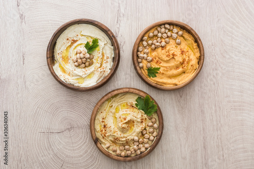 top view of delicious hummus with chickpeas in bowls on beige wooden table