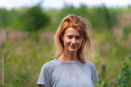 Redhead young girl stays in simple summer outfit outdoor on green natural background