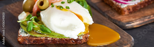 panoramic shot of smorrebrod sandwich with poached egg on wooden cutting board