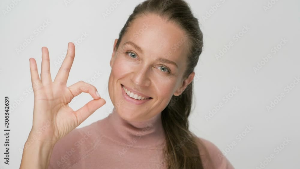 Happy brunette woman showing ok gesture looking at the camera and smile over white background Happy brunette woman showing ok gesture looking at the camera and smile over white background