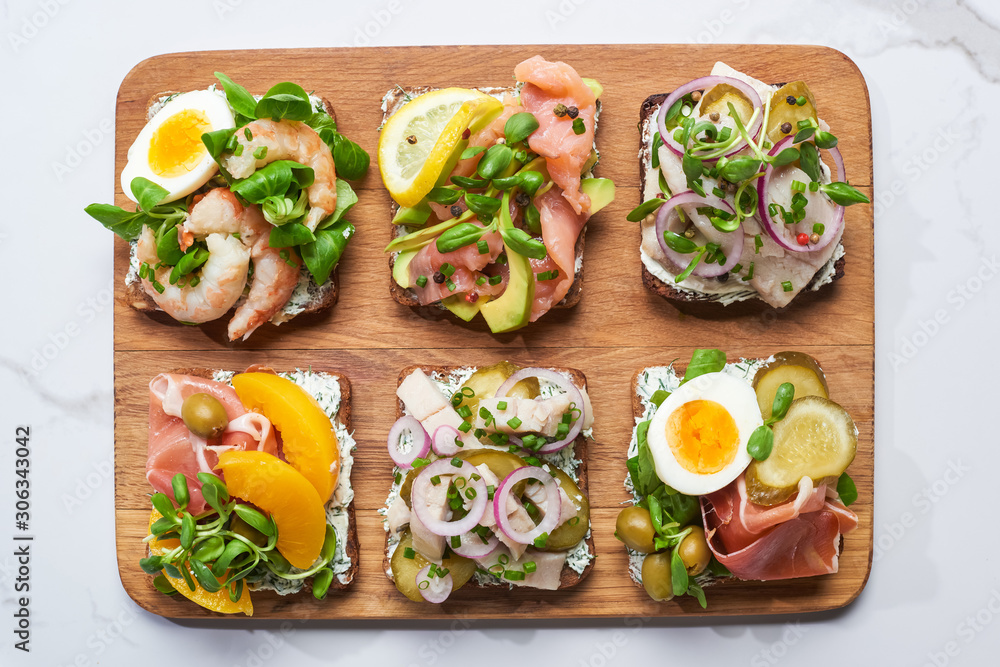 top view of wooden cutting board with tasty smorrebrod sandwiches on white marble surface top view of wooden cutting board with tasty smorrebrod sandwiches on white marble surface