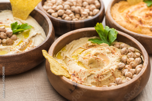 close up view of delicious hummus with chickpeas and nacho in bowls on beige wooden table