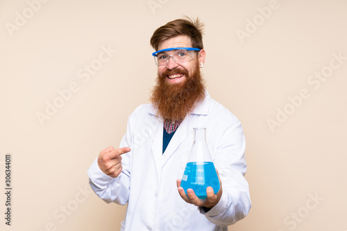 Redhead man with long beard over isolated background with a scientific test tube and pointing it
