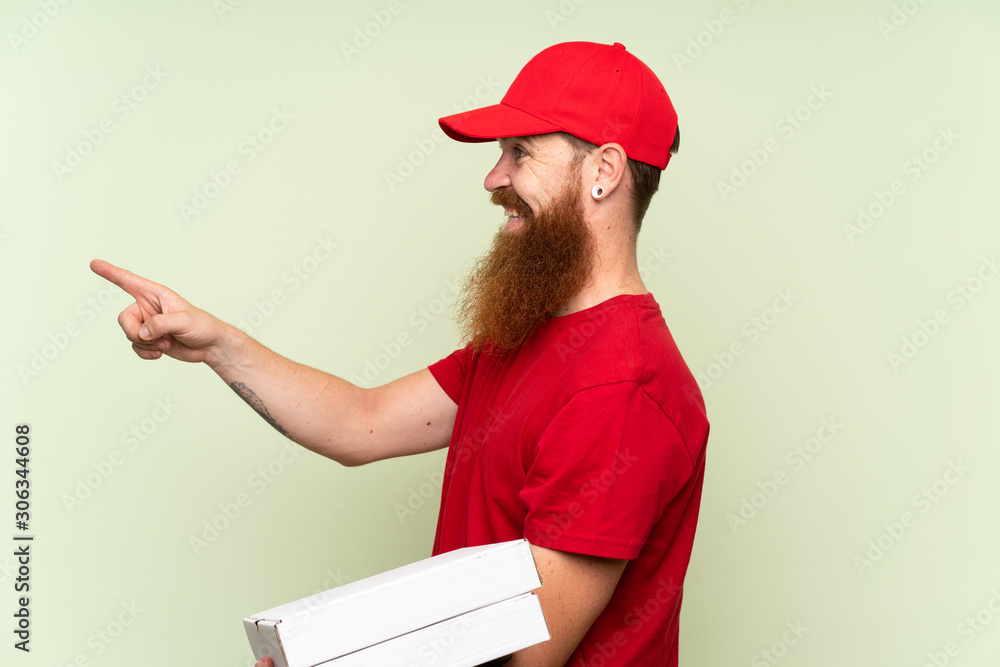 Delivery man with long beard over isolated green background pointing to the side to present a product Delivery man with long beard over isolated green background pointing to the side to present a product