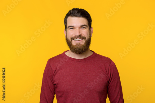 Portrait of bearded guy, wearing red sweater , smiling at camera, standing over yellow background