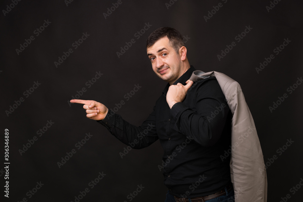 Portrait of business man looking at camer and pointing away from him, standing over dark background Portrait of business man looking at camer and pointing away from him, standing over dark background