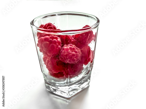 Glass cup filled with red raspberries, close-up, isolated on a white background. Ripe juicy red fruits in a transparent bowl, concept of organic juice and healthy food