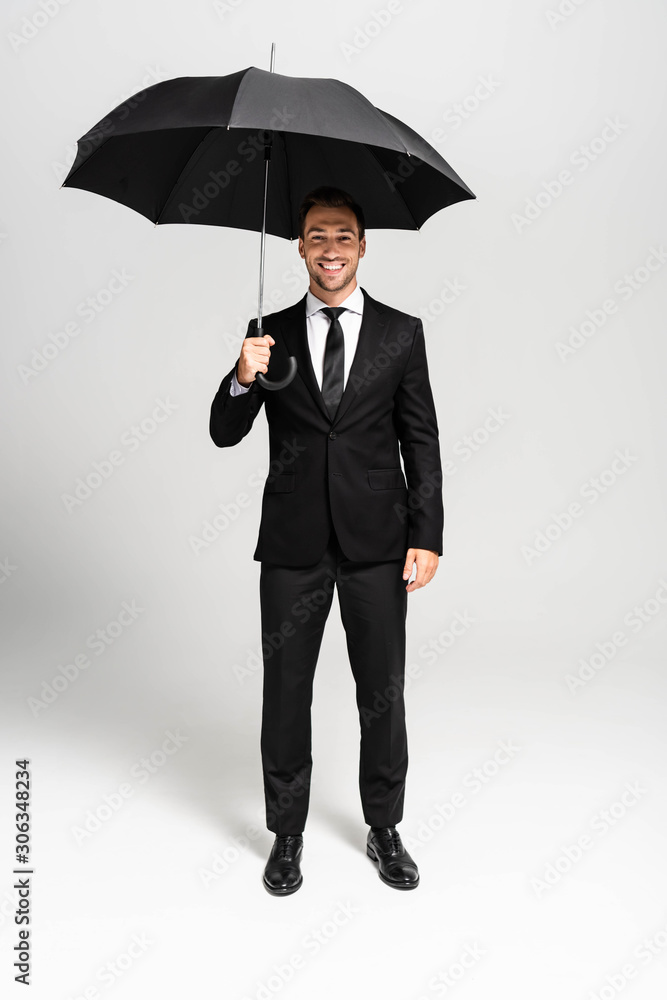 handsome and smiling businessman in suit holding umbrella on grey background handsome and smiling businessman in suit holding umbrella on grey background