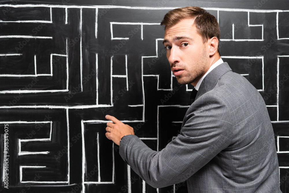 handsome and shocked businessman in suit pointing with finger at labyrinth handsome and shocked businessman in suit pointing with finger at labyrinth