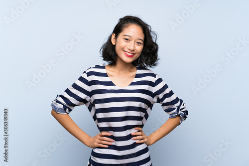 Asian young woman over isolated blue background posing with arms at hip and smiling