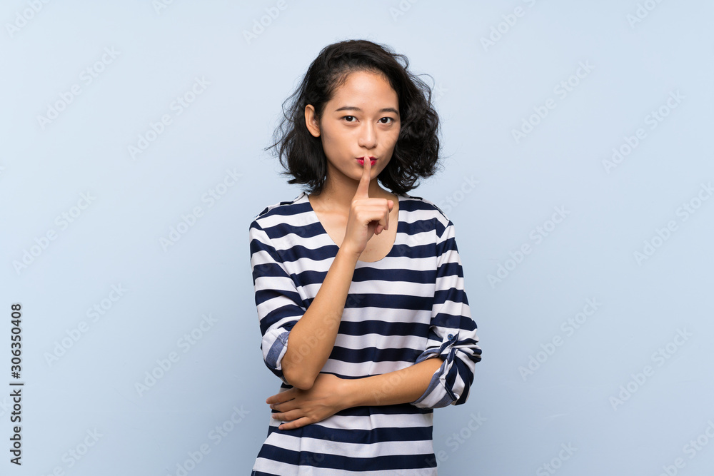 Asian young woman over isolated blue background showing a sign of silence gesture putting finger in mouth Asian young woman over isolated blue background showing a sign of silence gesture putting finger in mouth