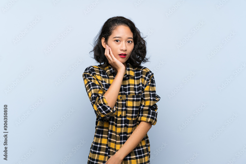 Asian young woman over isolated blue background surprised and shocked while looking right Asian young woman over isolated blue background surprised and shocked while looking right