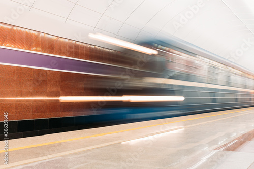Photo of blurred blue train entering the platform of the subway station. Metro platform decorated with marble of different colors. Public transport and mobility in urban concept.