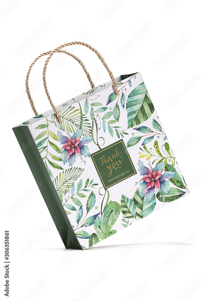 Subject shot of a white gift bag with silky plaited handles and decorated with colorful floral tropic print and with a pleasant text: 