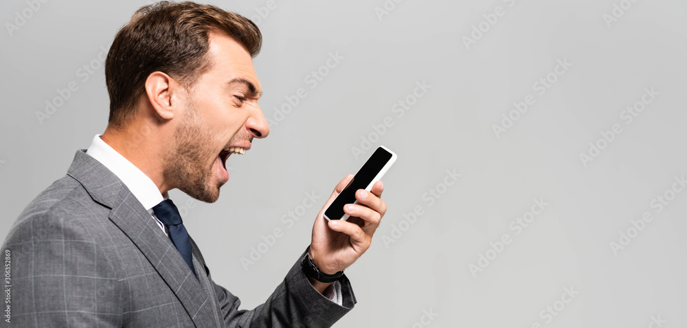 panoramic shot of handsome and angry businessman in suit shouting at smartphone isolated on grey panoramic shot of handsome and angry businessman in suit shouting at smartphone isolated on grey