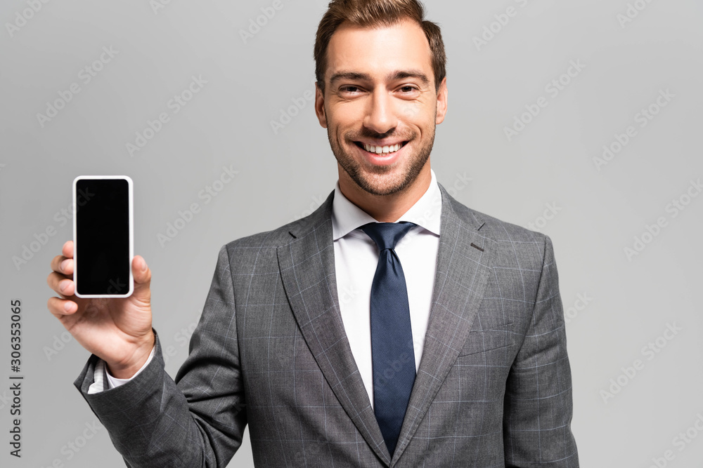handsome and smiling businessman in suit holding smartphone isolated on grey handsome and smiling businessman in suit holding smartphone isolated on grey